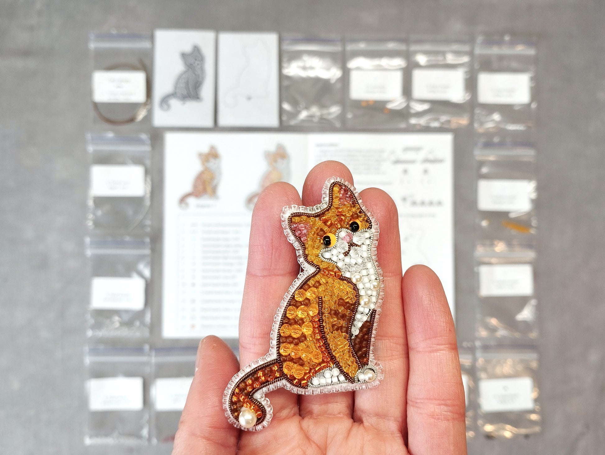A hand holding a small, intricately beaded cat pin.
