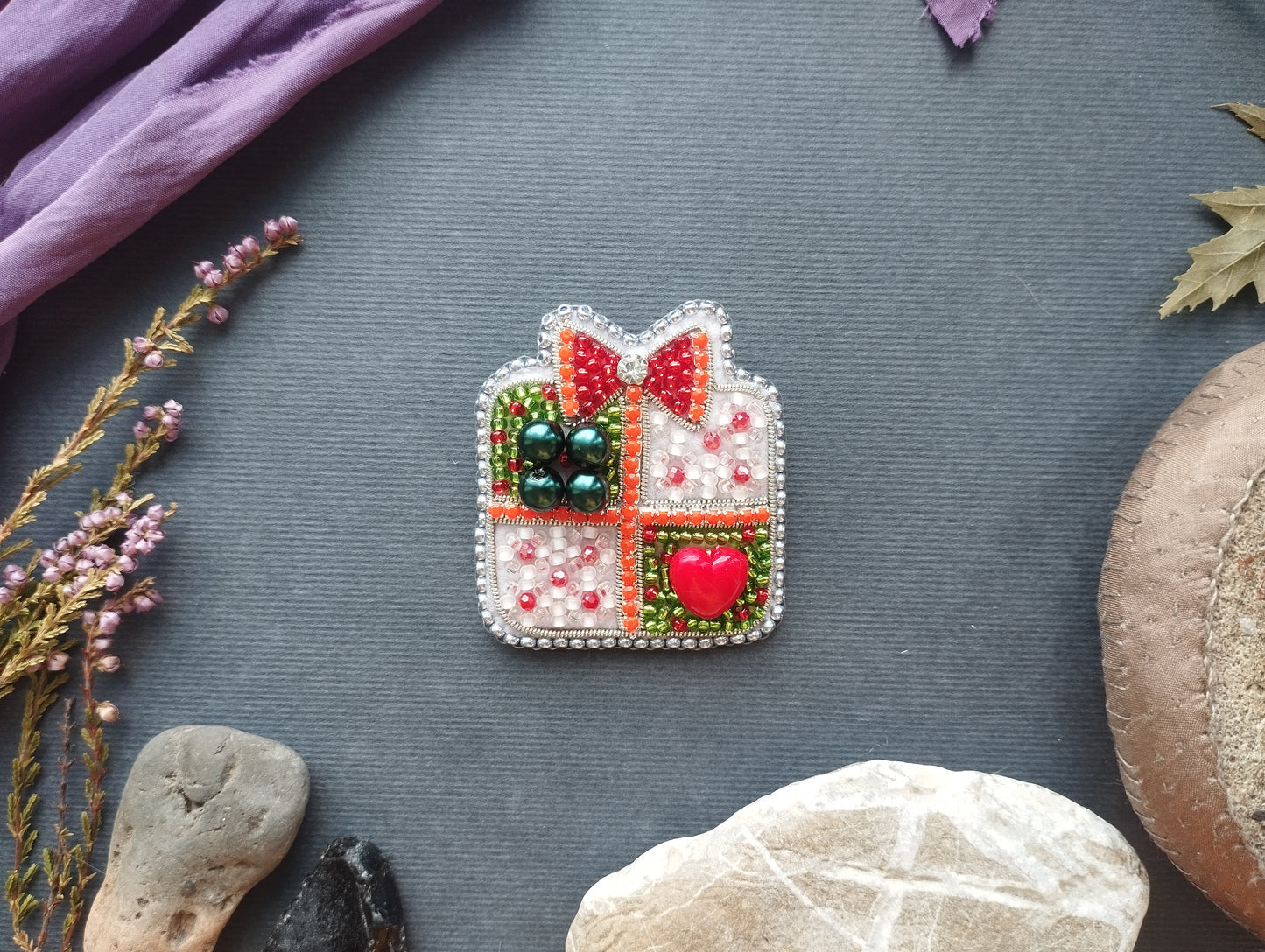 a decorative piece with a bow and heart, surrounded by various natural elements such as leaves, flowers, and rocks.