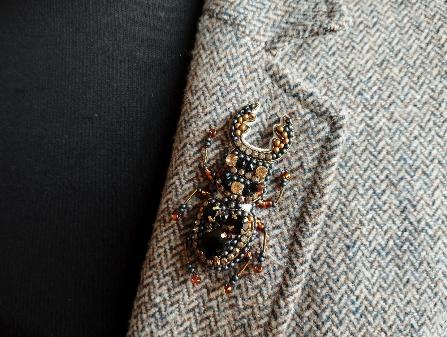 A close-up image of a decorative brooch or pin with a detailed design, placed on a textured fabric surface.