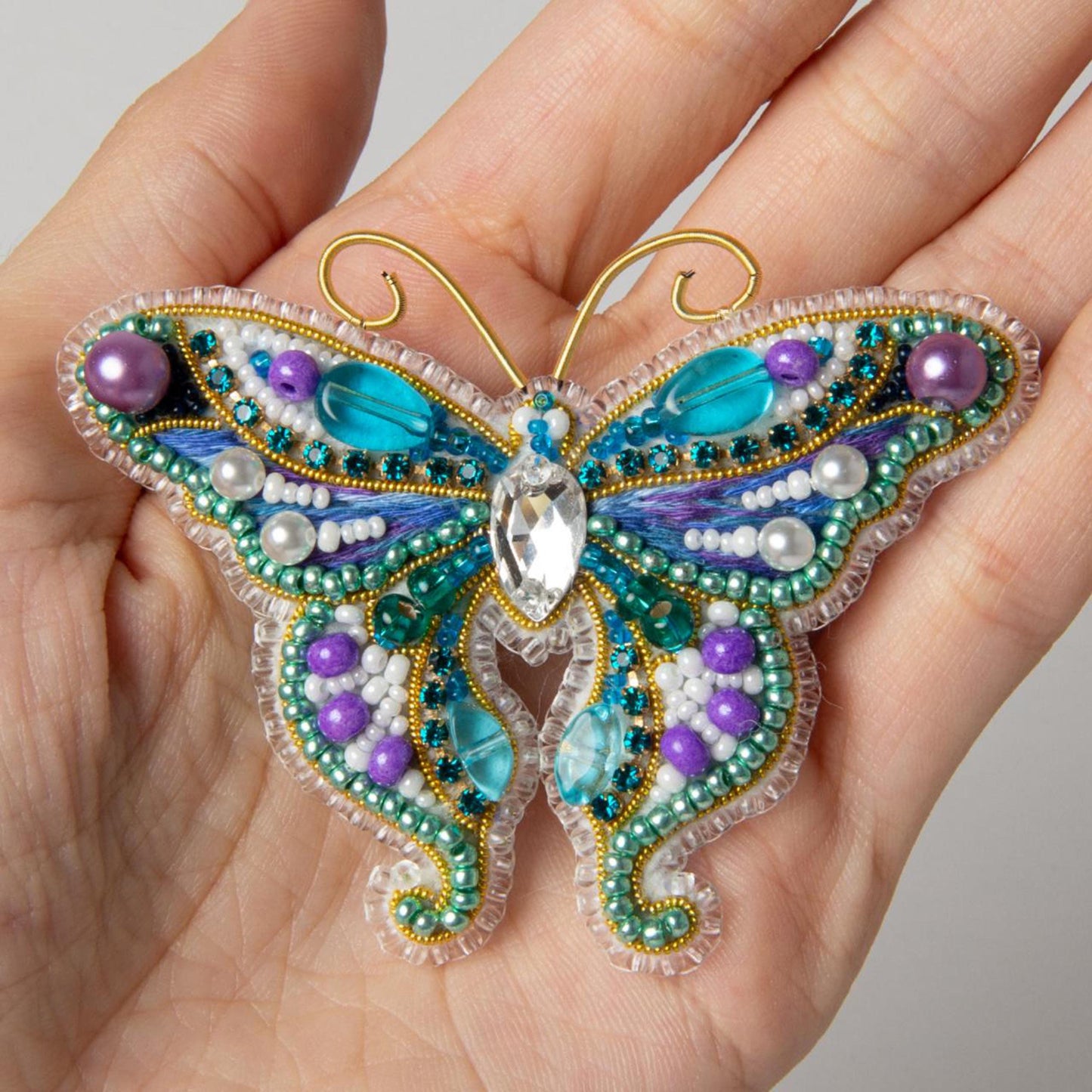 a hand is holding a beaded butterfly ornament