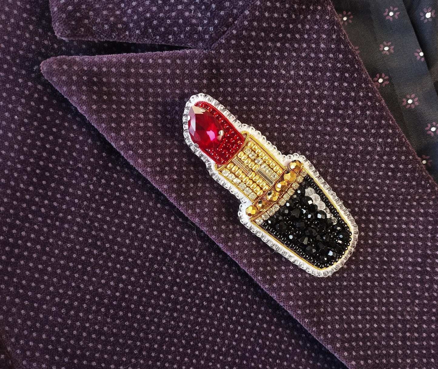 A close-up image of a purple fabric with a decorative red and gold pin featuring a red lipstick design.