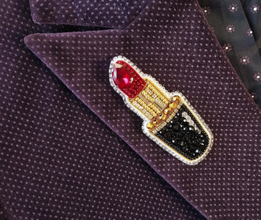 A close-up image of a purple fabric with a decorative red and gold pin featuring a red lipstick design.
