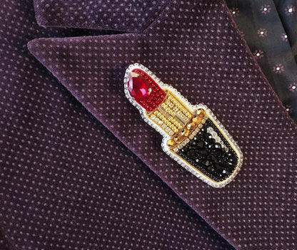 A close-up image of a purple fabric with a decorative red and gold pin featuring a red lipstick design.