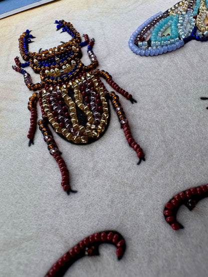a close-up view of a detailed embroidered design of a large insect, possibly a beetle, with intricate patterns and beadwork.