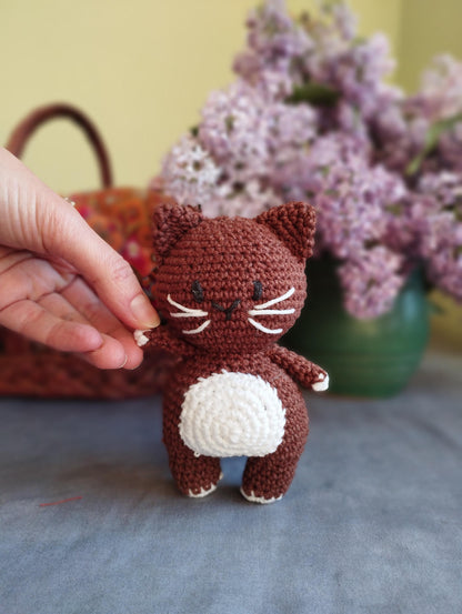 a crocheted cat sitting on a table next to a basket of flowers
