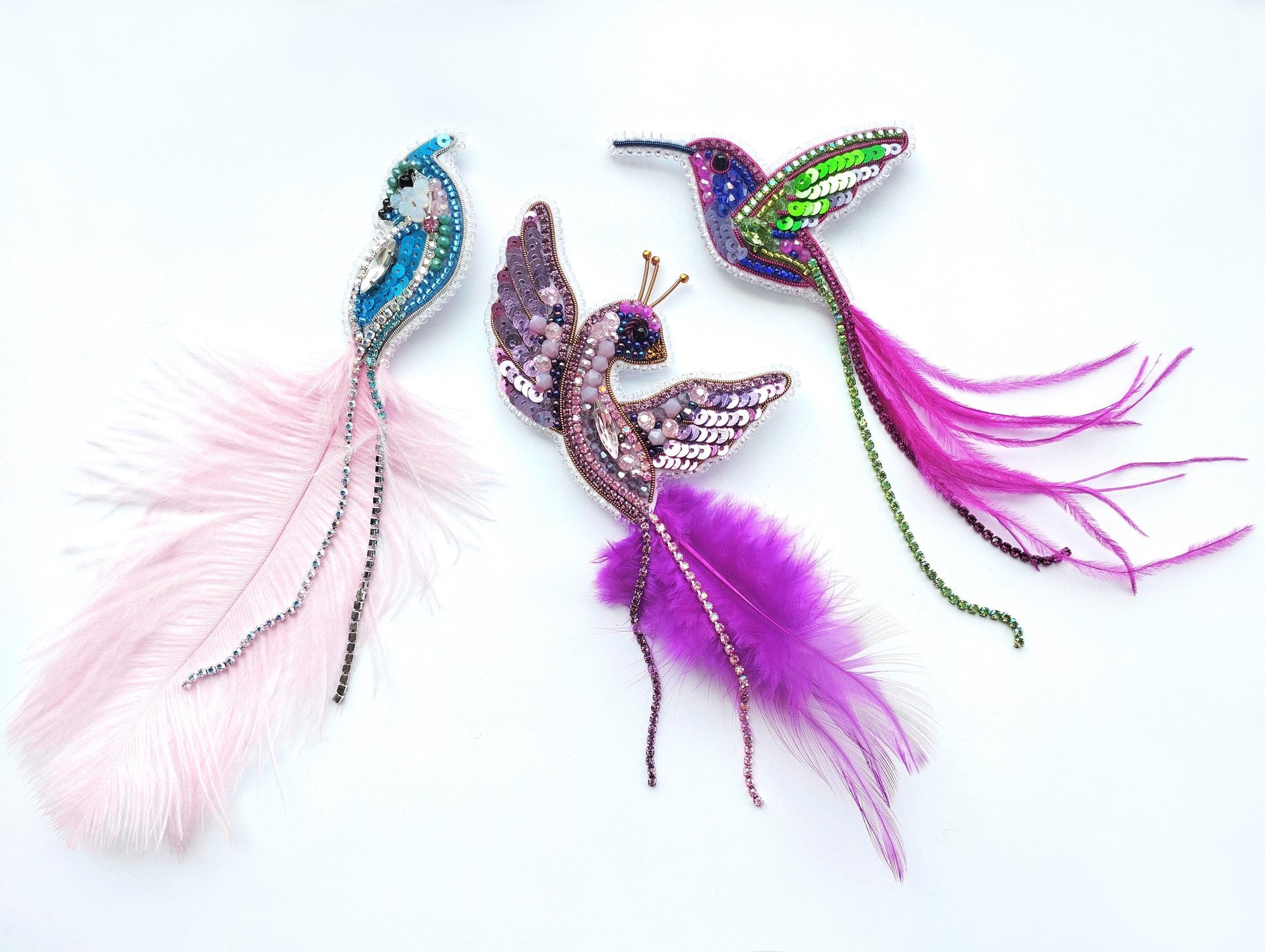 three colorful, intricately designed bird-shaped brooches or pendants, each with unique feather patterns and embellishments.