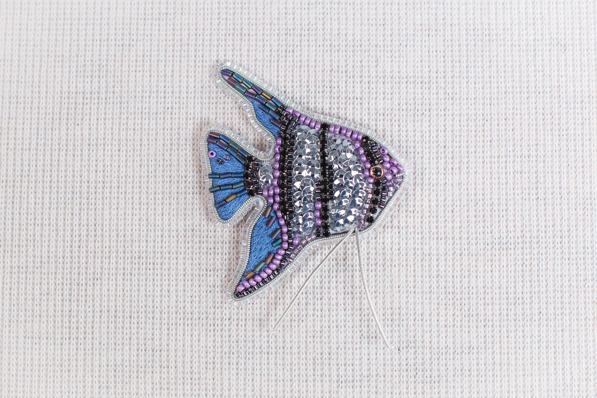 A colorful, intricately designed fish-shaped object made of beads and other materials, placed on a plain white background.