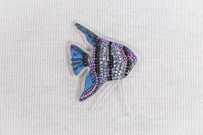A colorful, intricately designed fish-shaped object made of beads and other materials, placed on a plain white background.