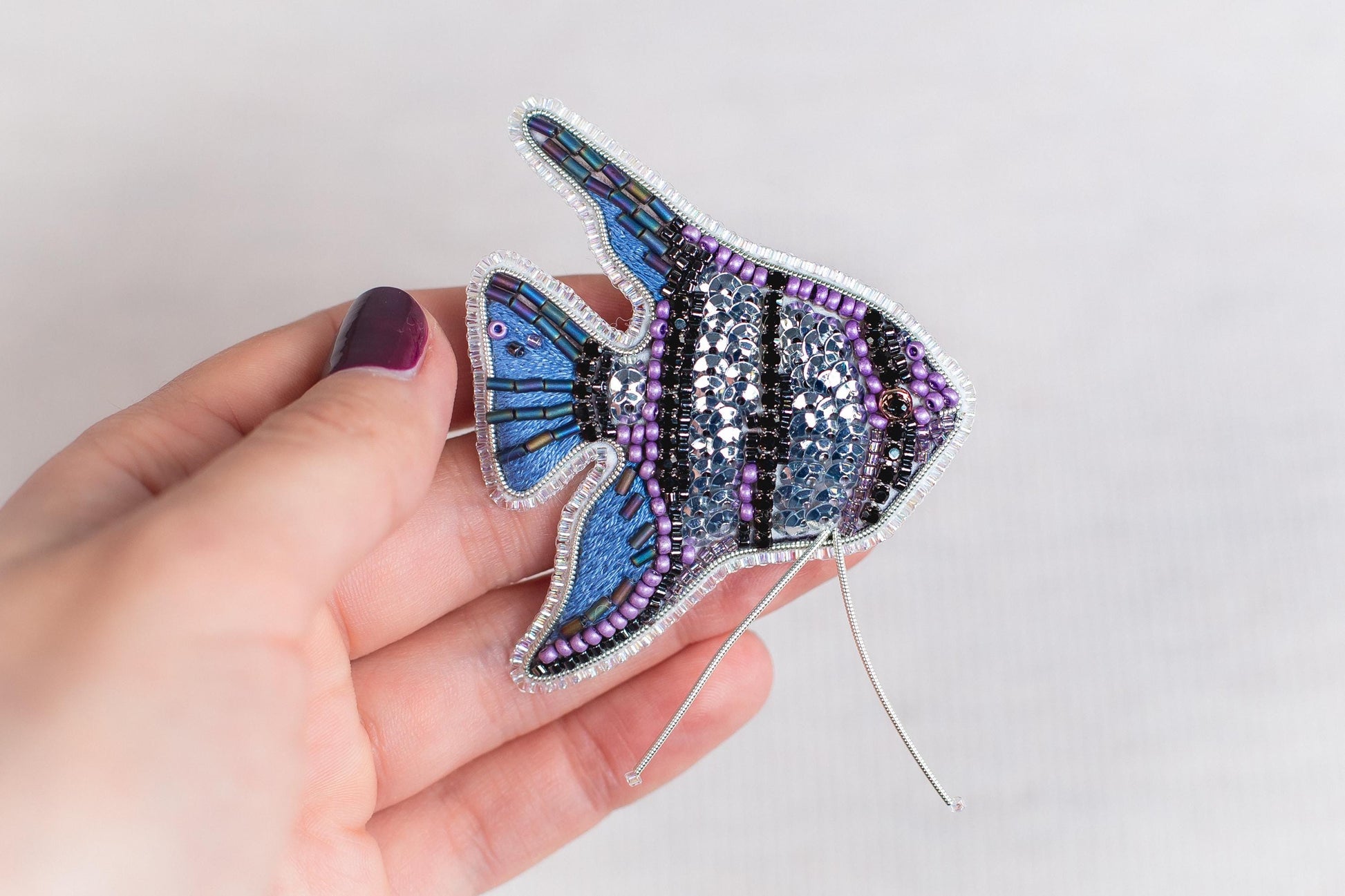 A hand holding a decorative fish-shaped brooch made of colorful beads and wire.