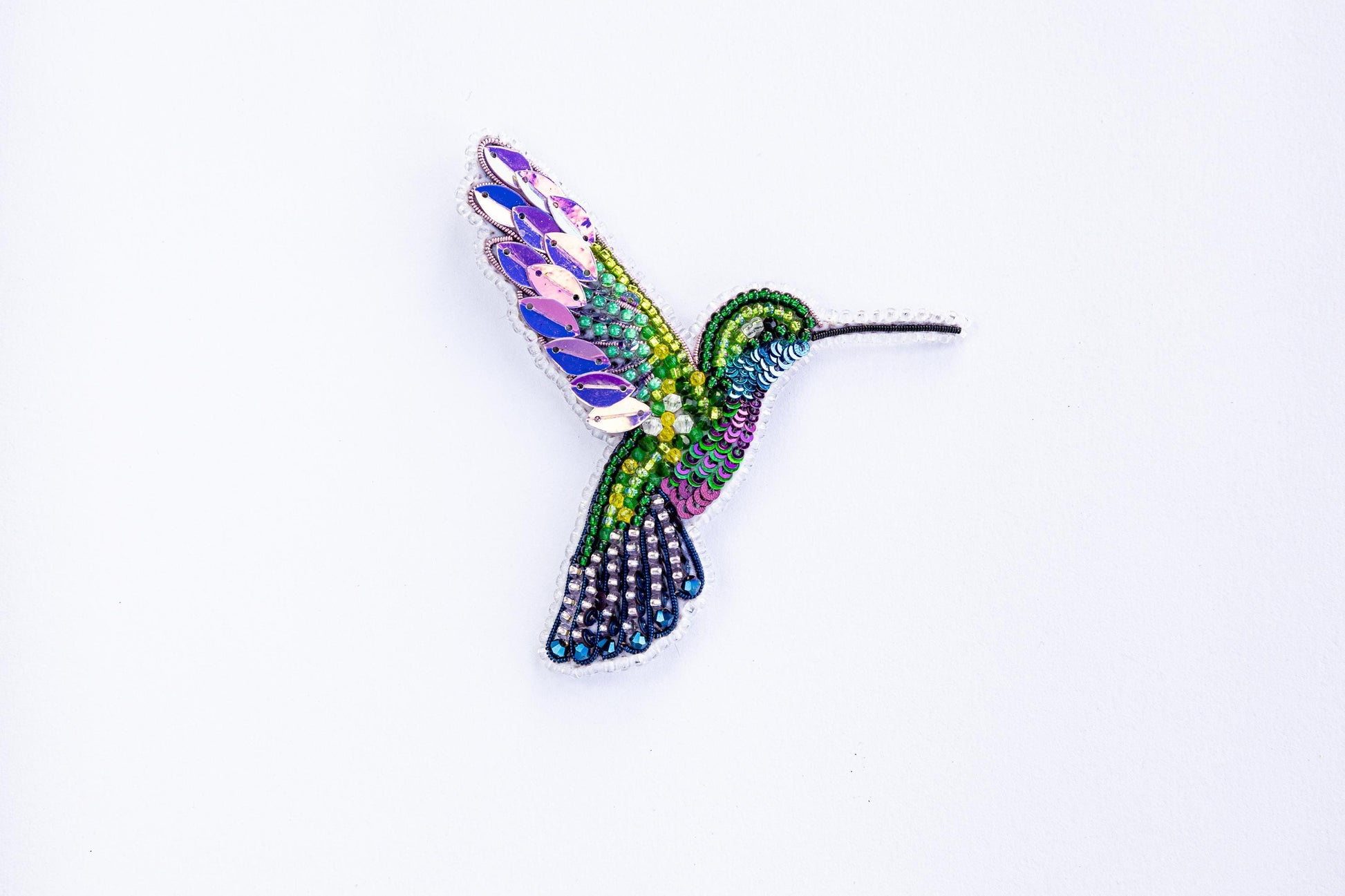 a colorful hummingbird brooch sitting on top of a white surface