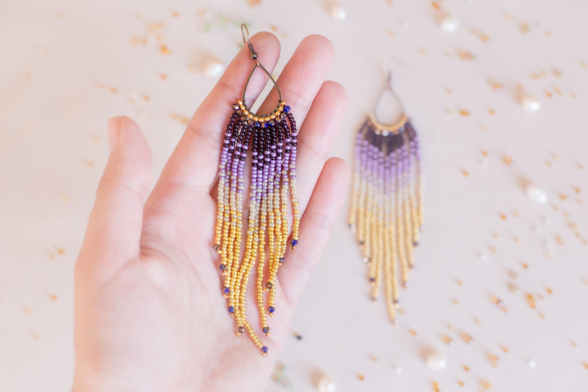 a hand holding a pair of beaded earrings