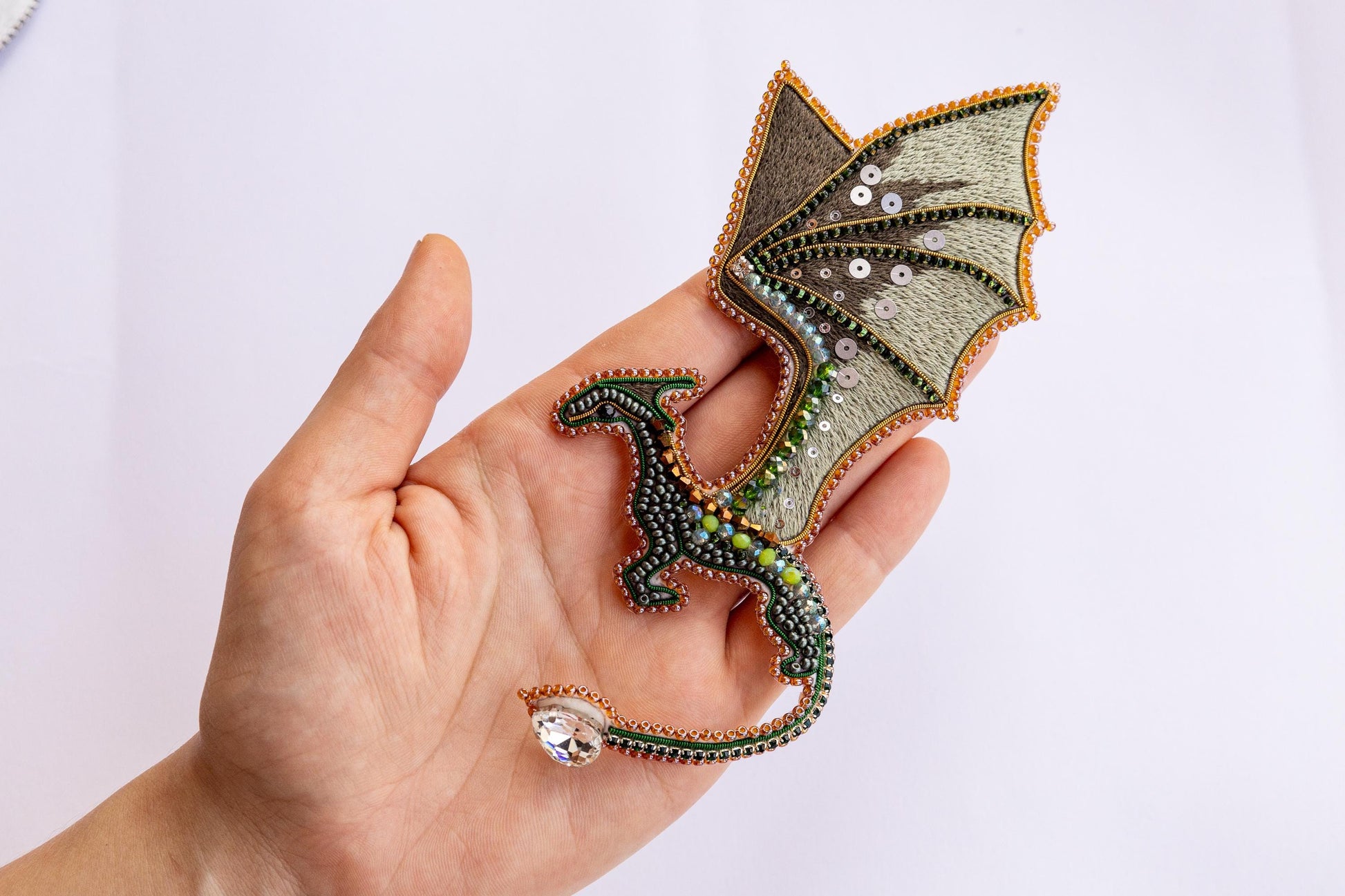 a hand holding a small green dragon brooch