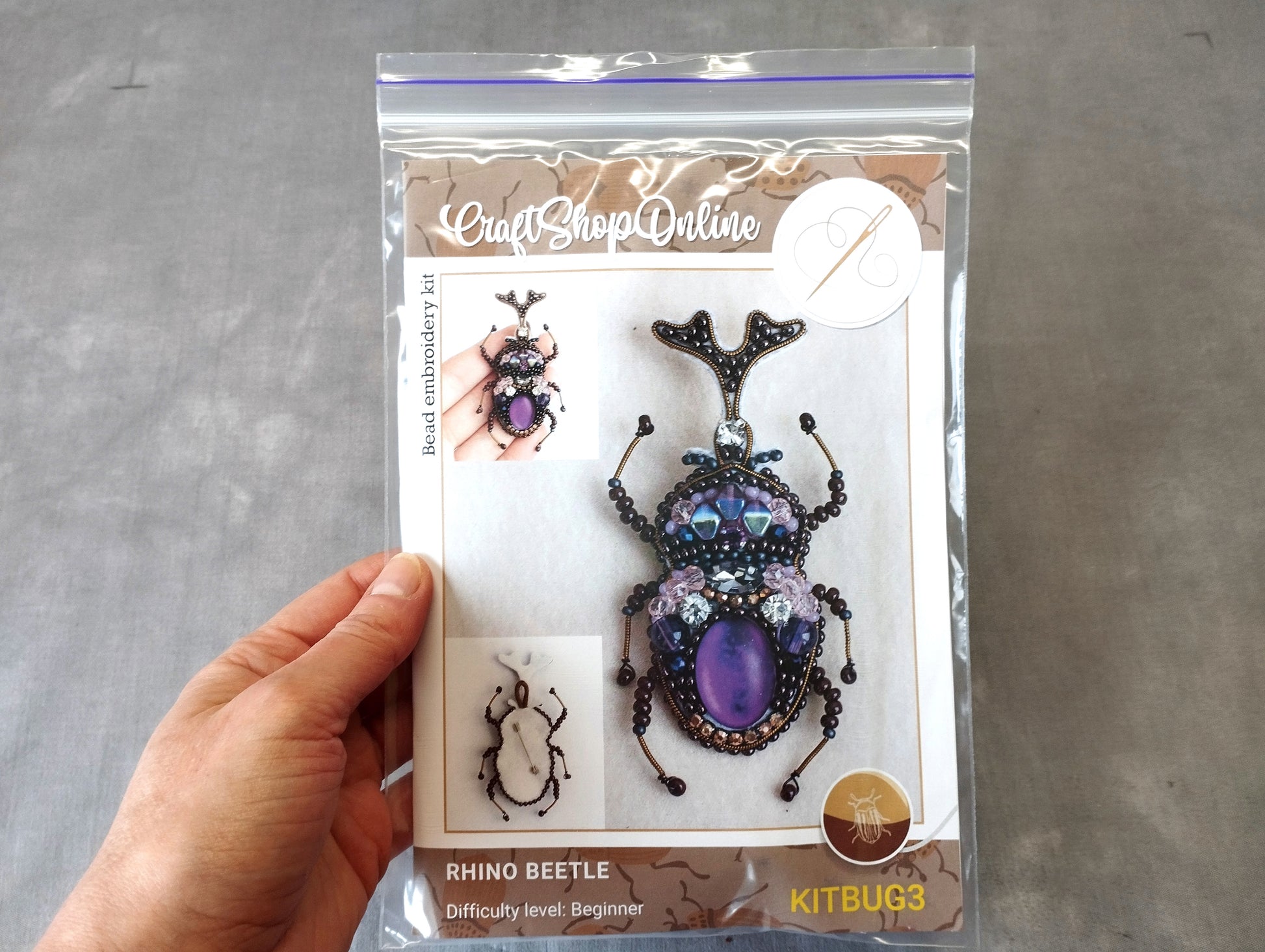 A hand is holding a package containing a rhino beetle bead embroidery kit.