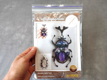 A hand is holding a package containing a rhino beetle bead embroidery kit.