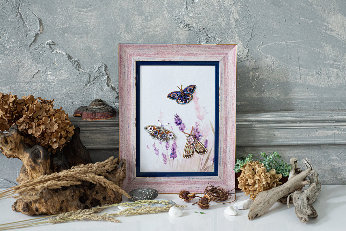 a framed painting of butterflies on a white background, surrounded by various natural elements such as dried flowers, driftwood, and rocks.