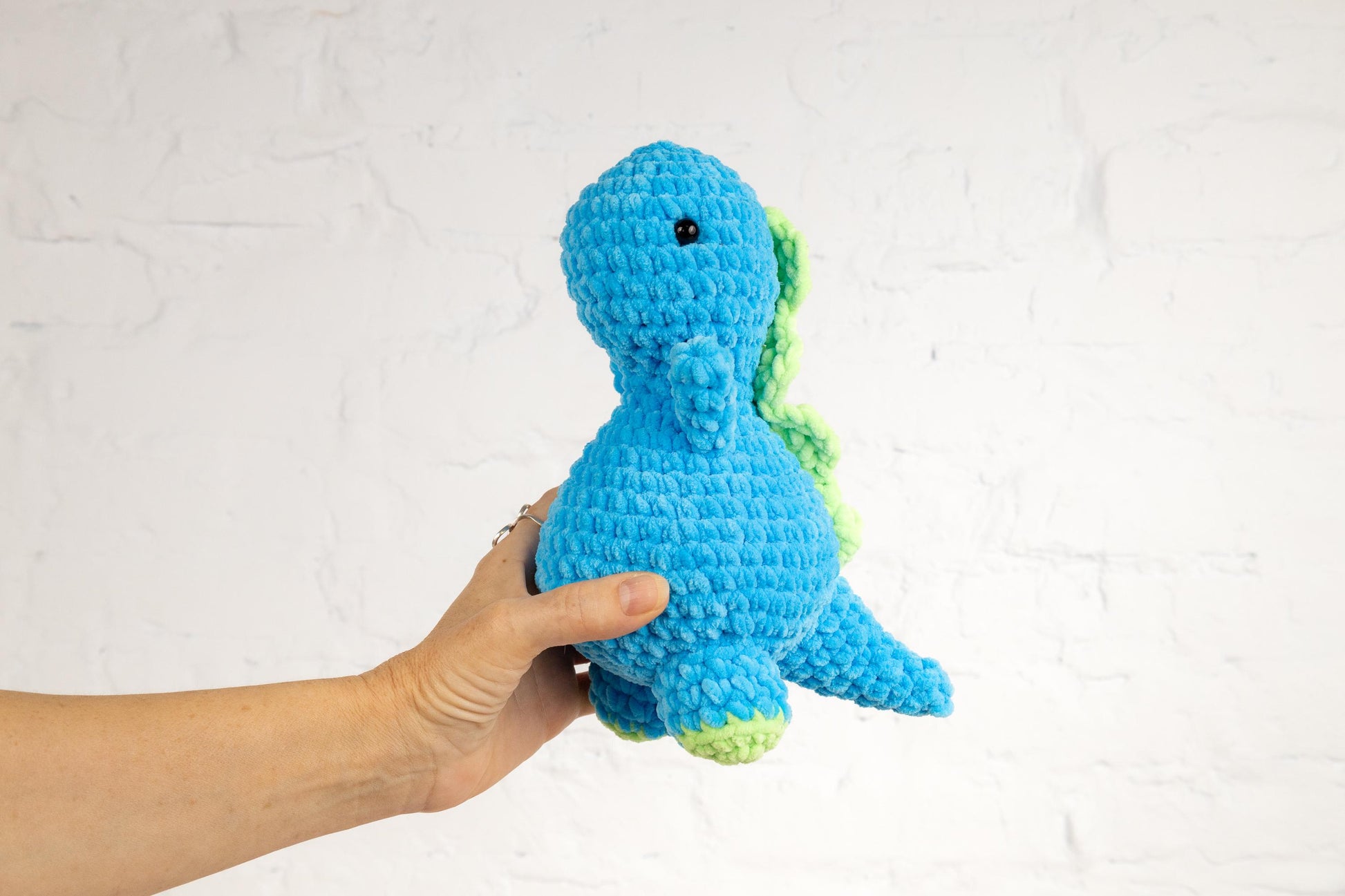 a hand holding a small blue crocheted toy
