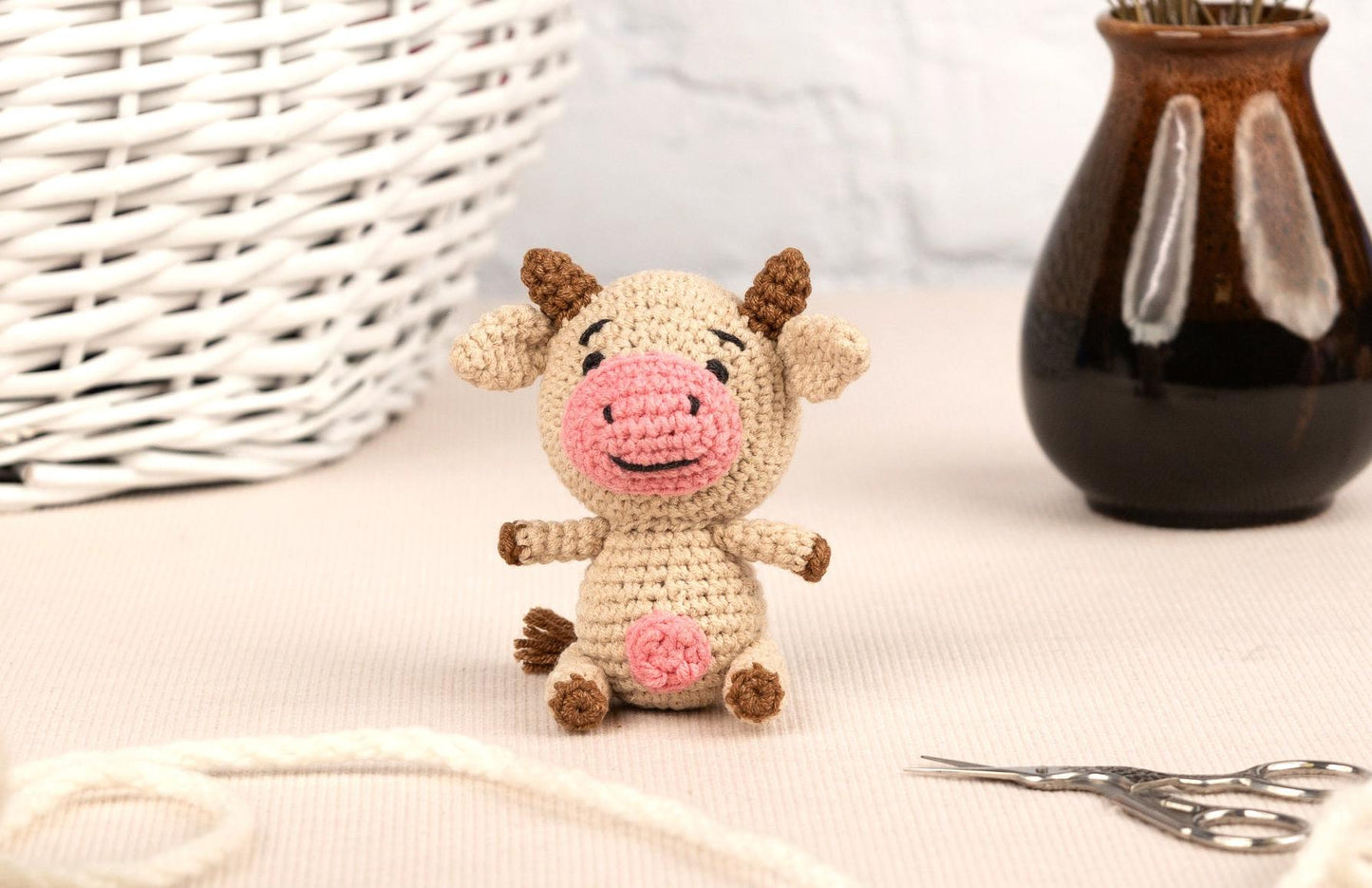 a small crocheted pig sitting next to a brown vase