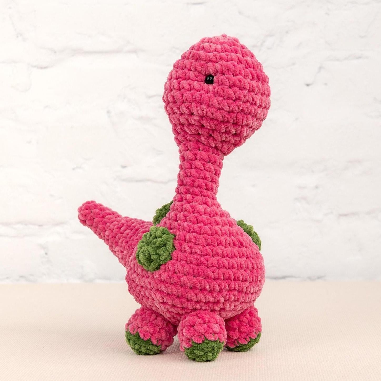 a crocheted pink dinosaur sitting on a table