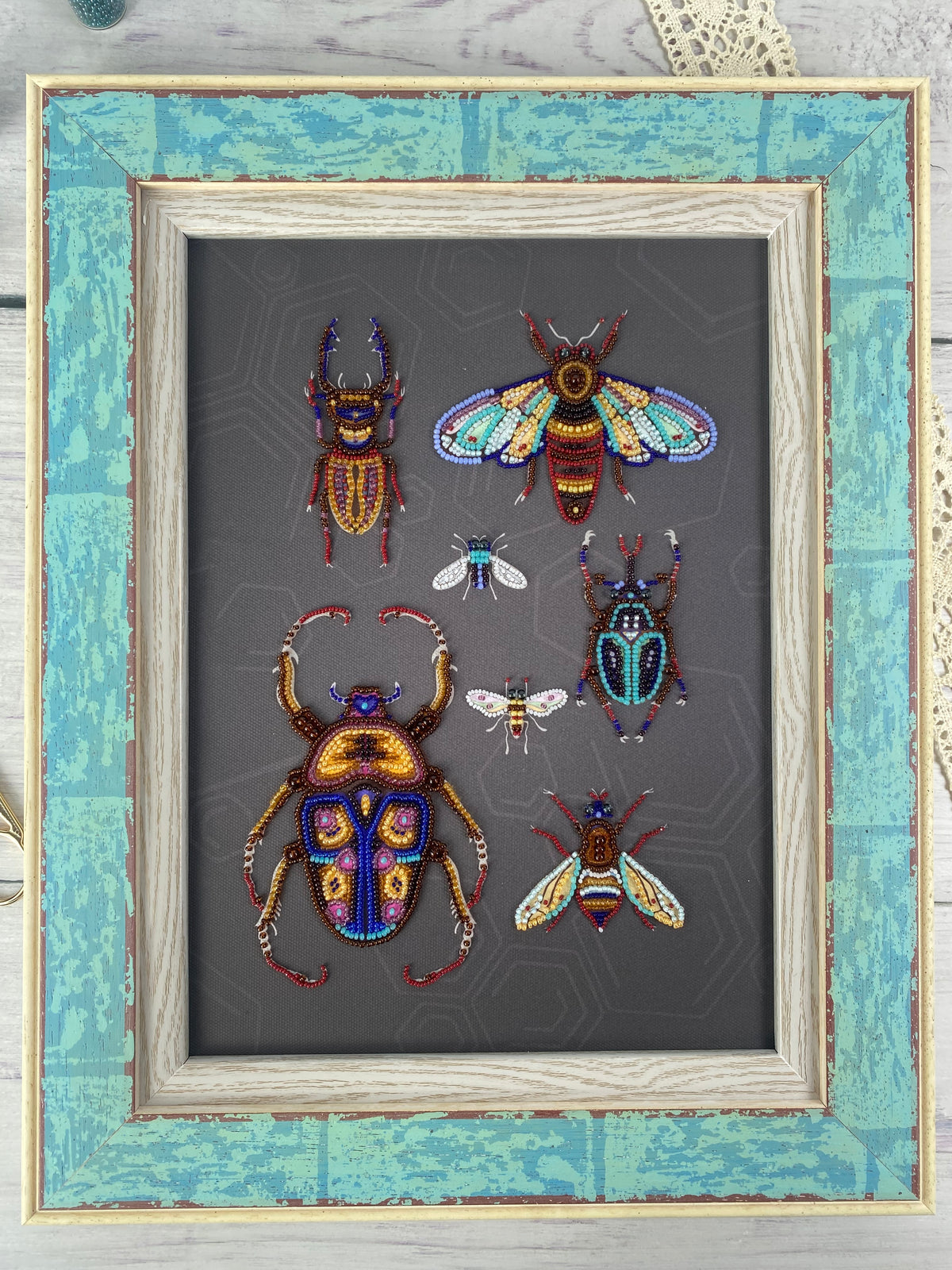 a framed collection of six intricately detailed and colorful insects, including a large dragonfly, a group of bees, and a variety of other insects, all set against a dark background.