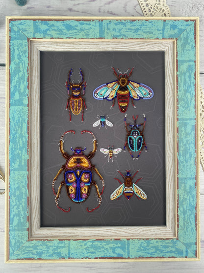 a framed collection of six intricately detailed and colorful insects, including a large dragonfly, a group of bees, and a variety of other insects, all set against a dark background.