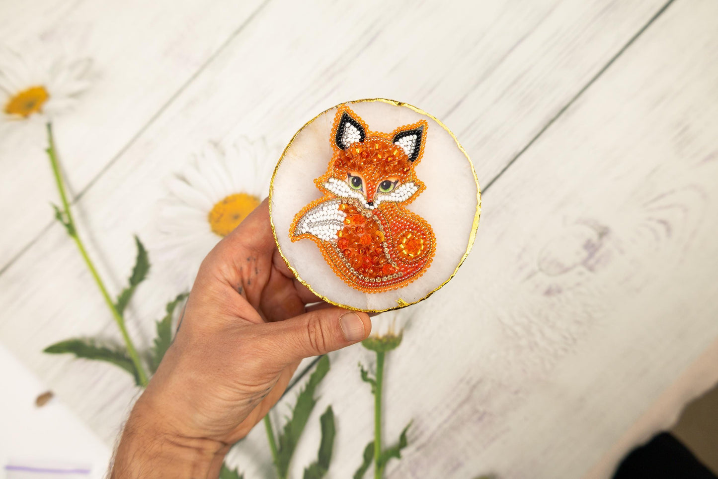 a hand holding a small embroidered brooch with a picture of a fox on it