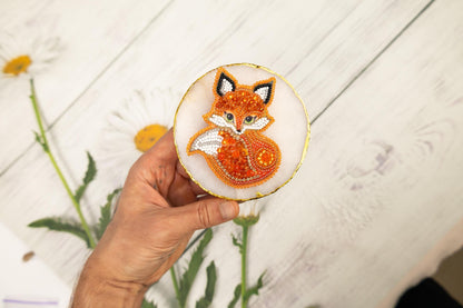 a hand holding a small embroidered brooch with a picture of a fox on it