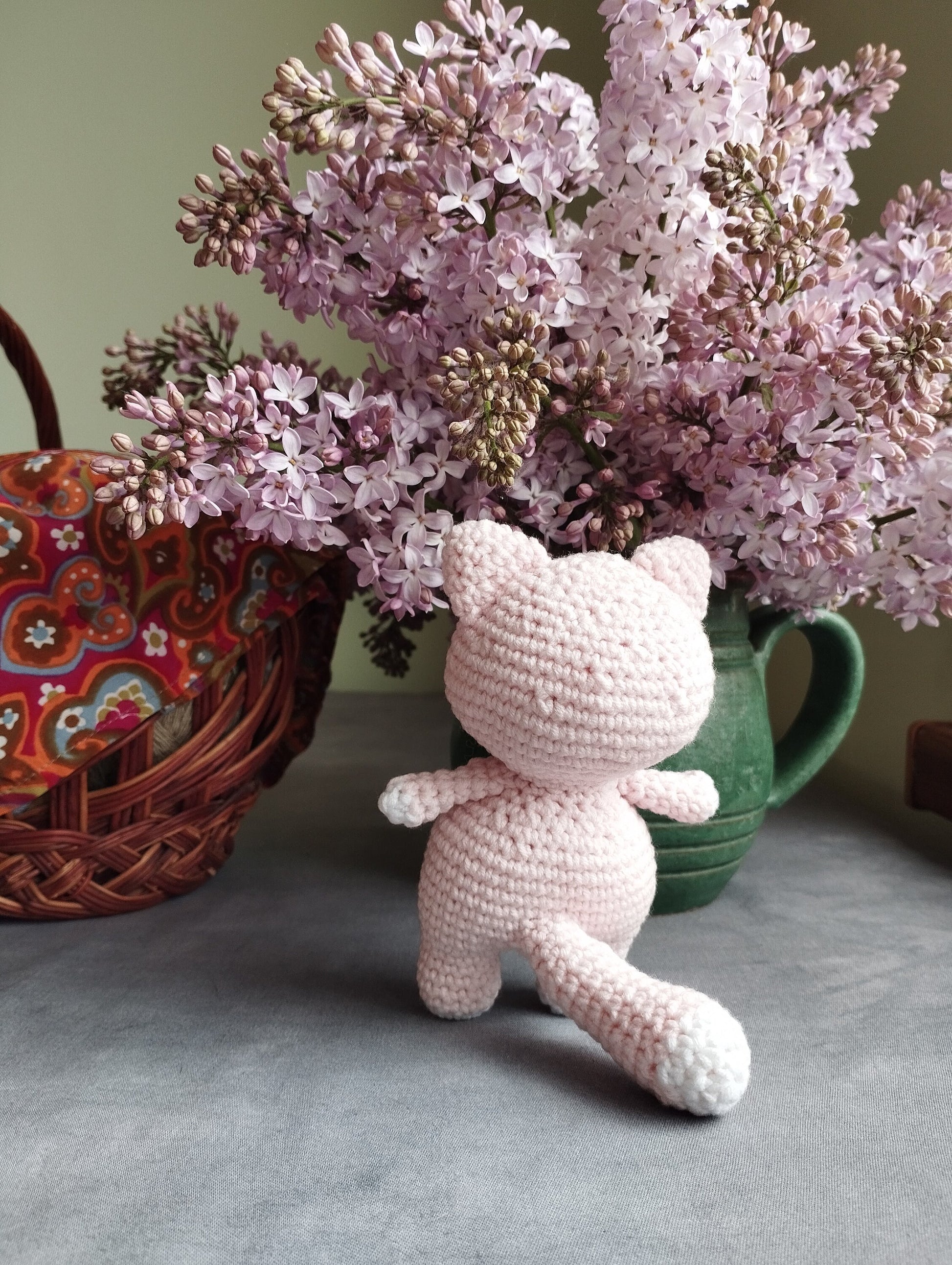 a crocheted teddy bear sitting next to a vase of lilacs
