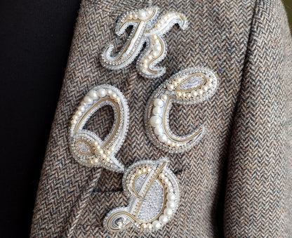 a close-up of a person's arm wearing a tweed jacket with a decorative embroidered letter on it.