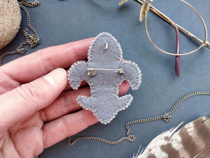 A hand holding a gray felt badge with a pin, surrounded by various accessories such as glasses, a chain, and feathers.