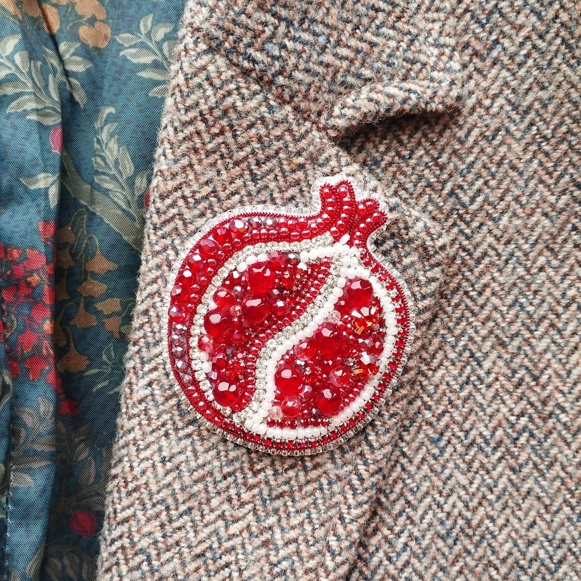 a close-up view of a pomegranate-shaped embroidered piece on a tweed jacket.