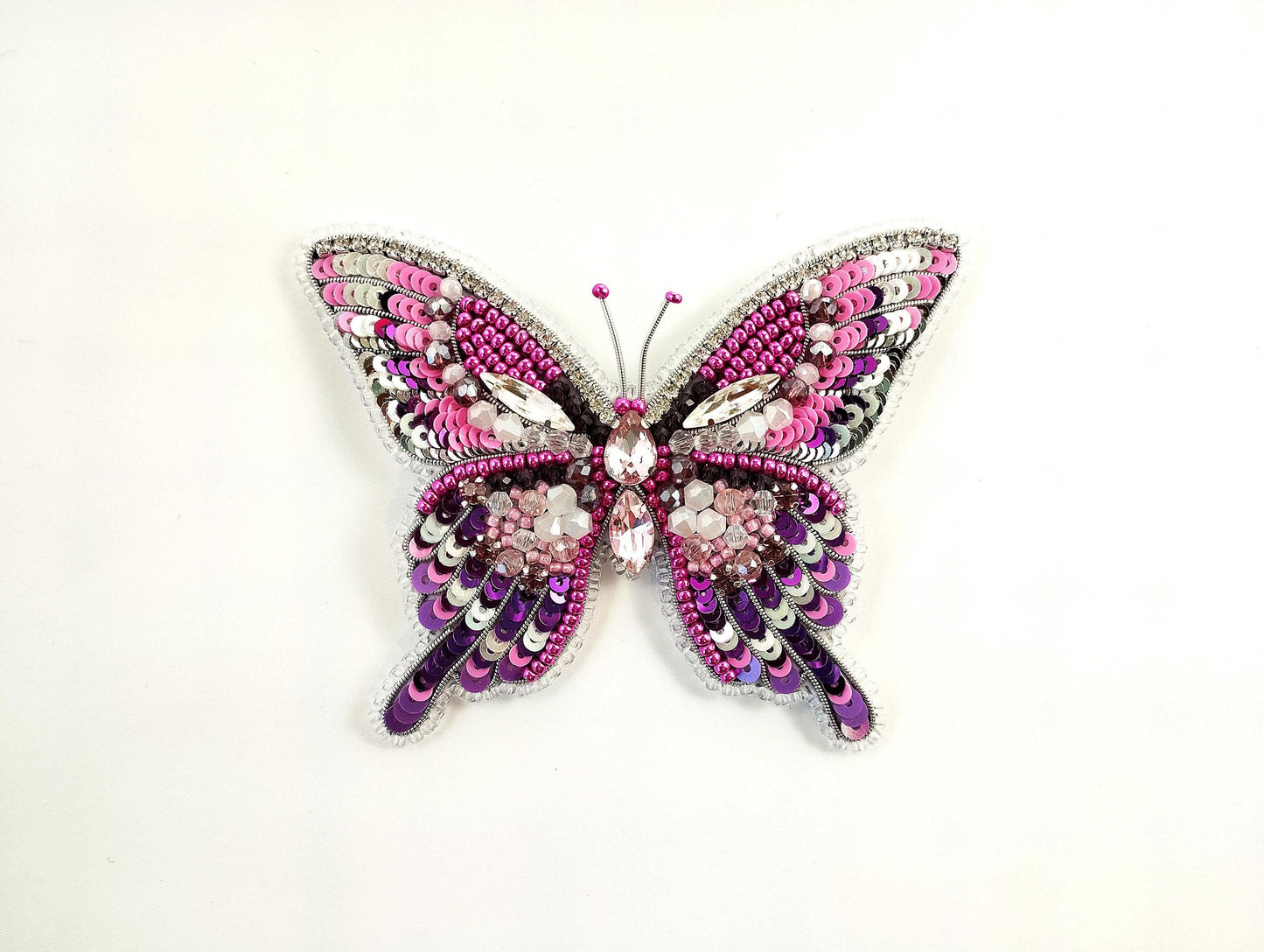 a pink and purple butterfly brooch sitting on top of a white surface