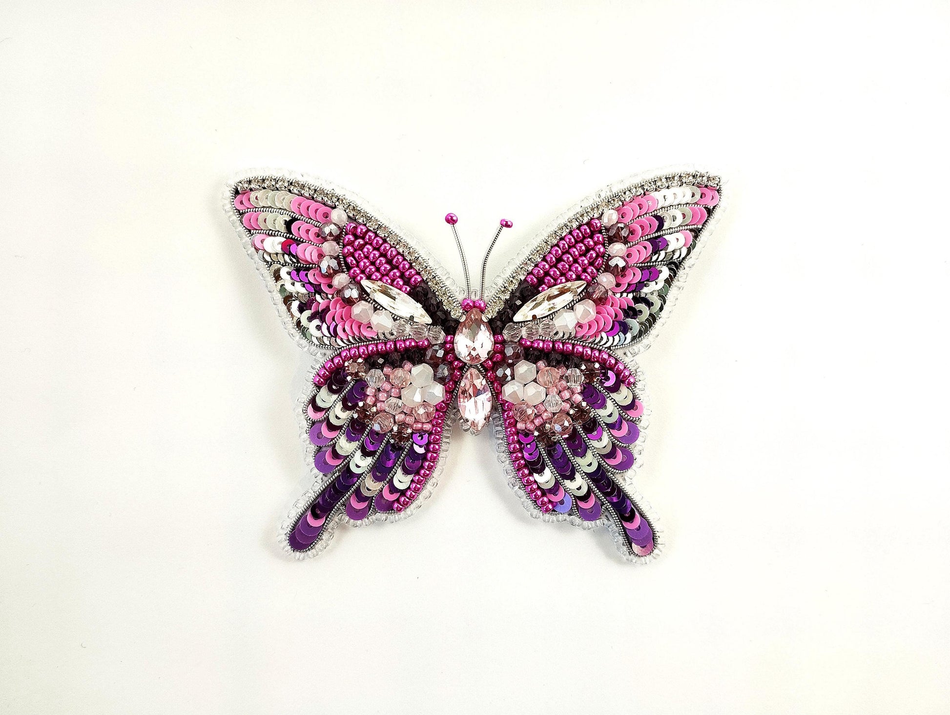 a pink and purple butterfly brooch sitting on top of a white surface