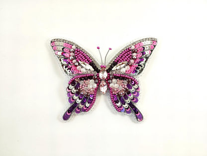 a pink and purple butterfly brooch sitting on top of a white surface