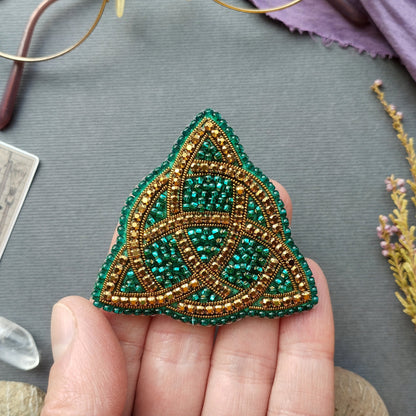 A hand holding a triangular beaded object with a green and gold color scheme.