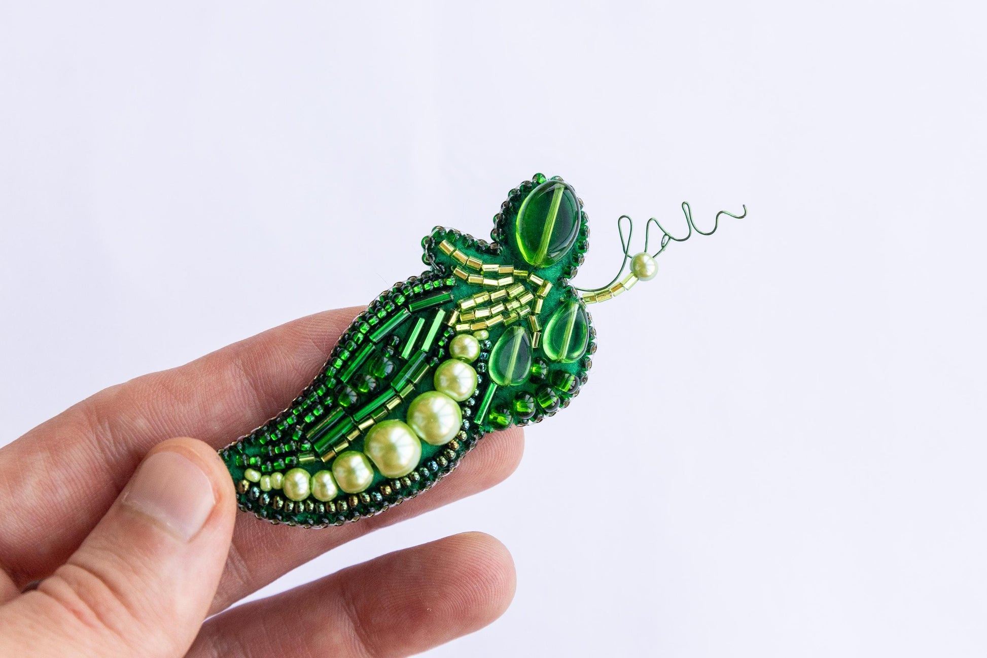 a hand holding a green beaded brooch