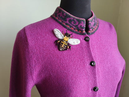 A close-up image of a woman wearing a purple sweater with a decorative bee embroidered on the front.