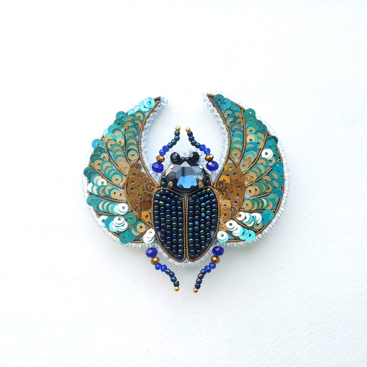 A decorative piece featuring a detailed embroidered design of a colorful insect, possibly a beetle or a fly, with intricate patterns and embellishments.
