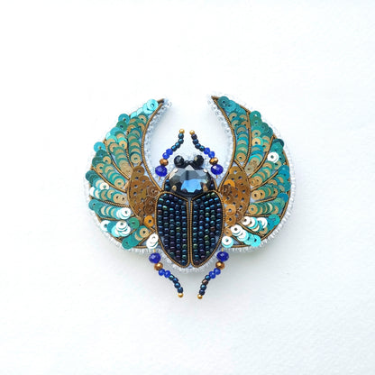 A decorative piece featuring a detailed embroidered design of a colorful insect, possibly a beetle or a fly, with intricate patterns and embellishments.