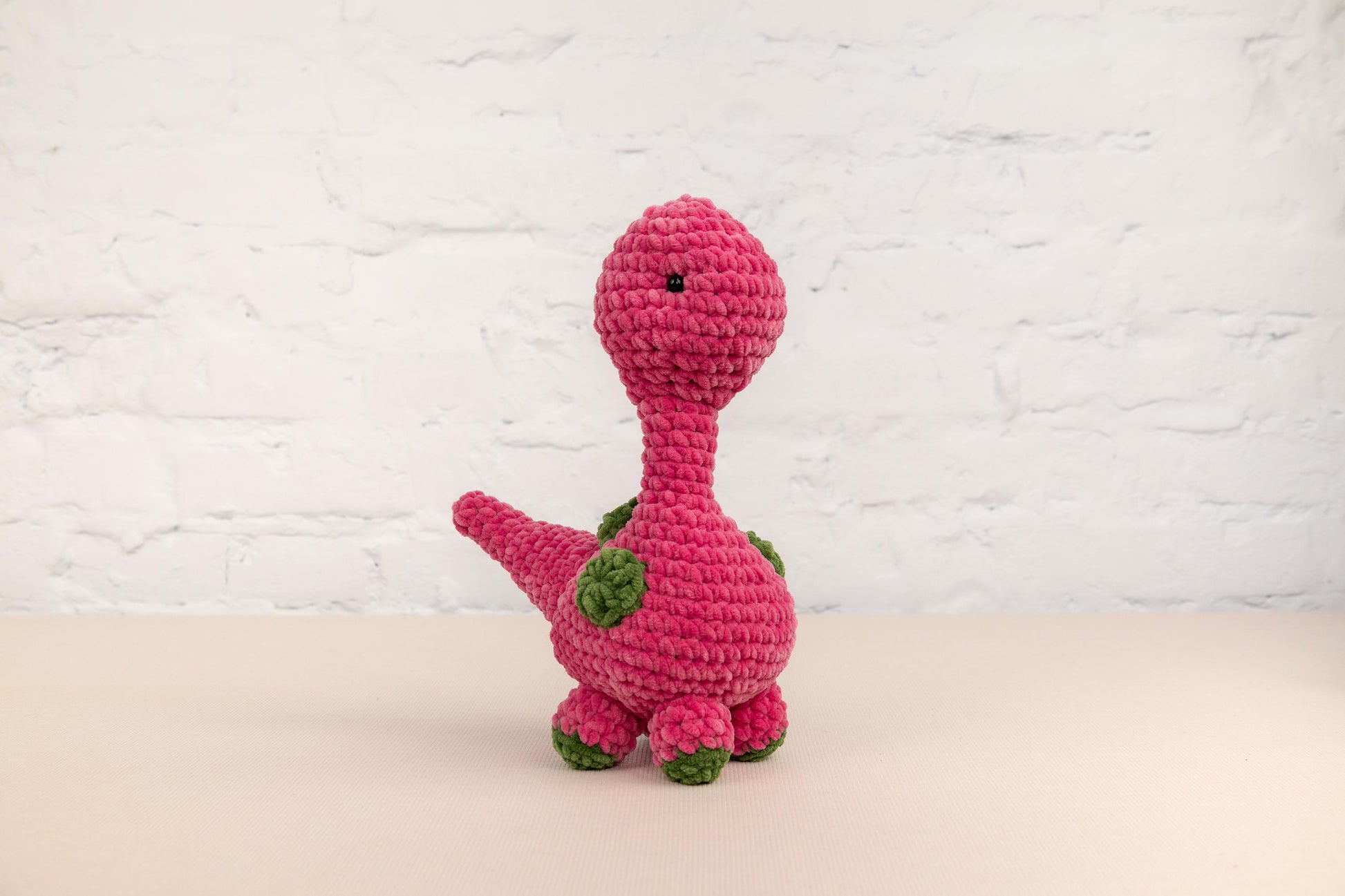 a pink crocheted dinosaur sitting on top of a table