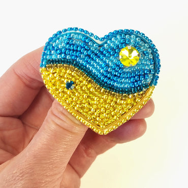 a hand holding a beaded heart shaped brooch