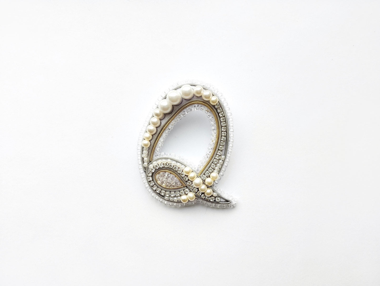 A decorative letter 'Q' made of pearls, diamonds, and other embellishments, displayed against a white background.