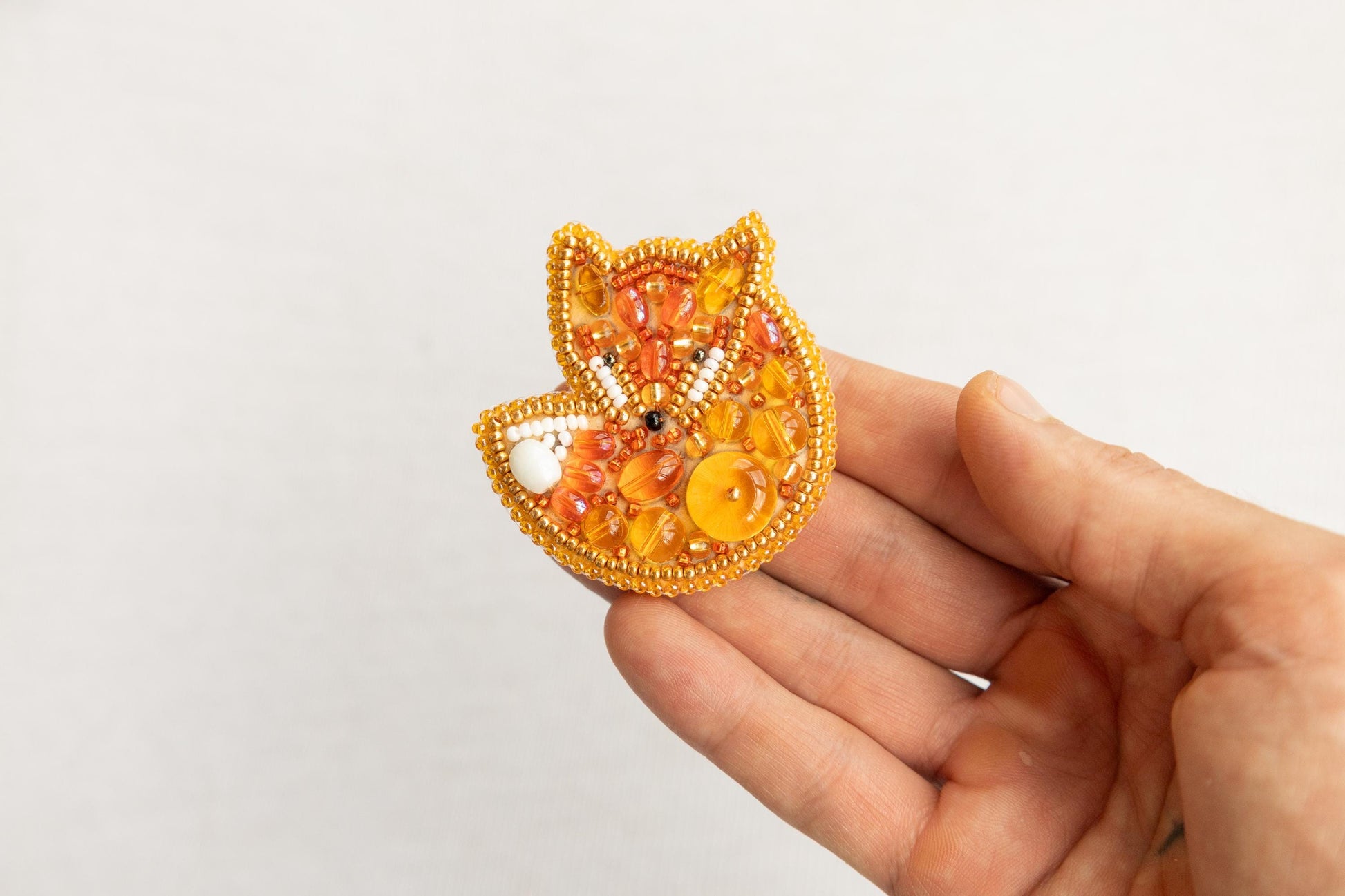 a hand is holding a beaded fox brooch