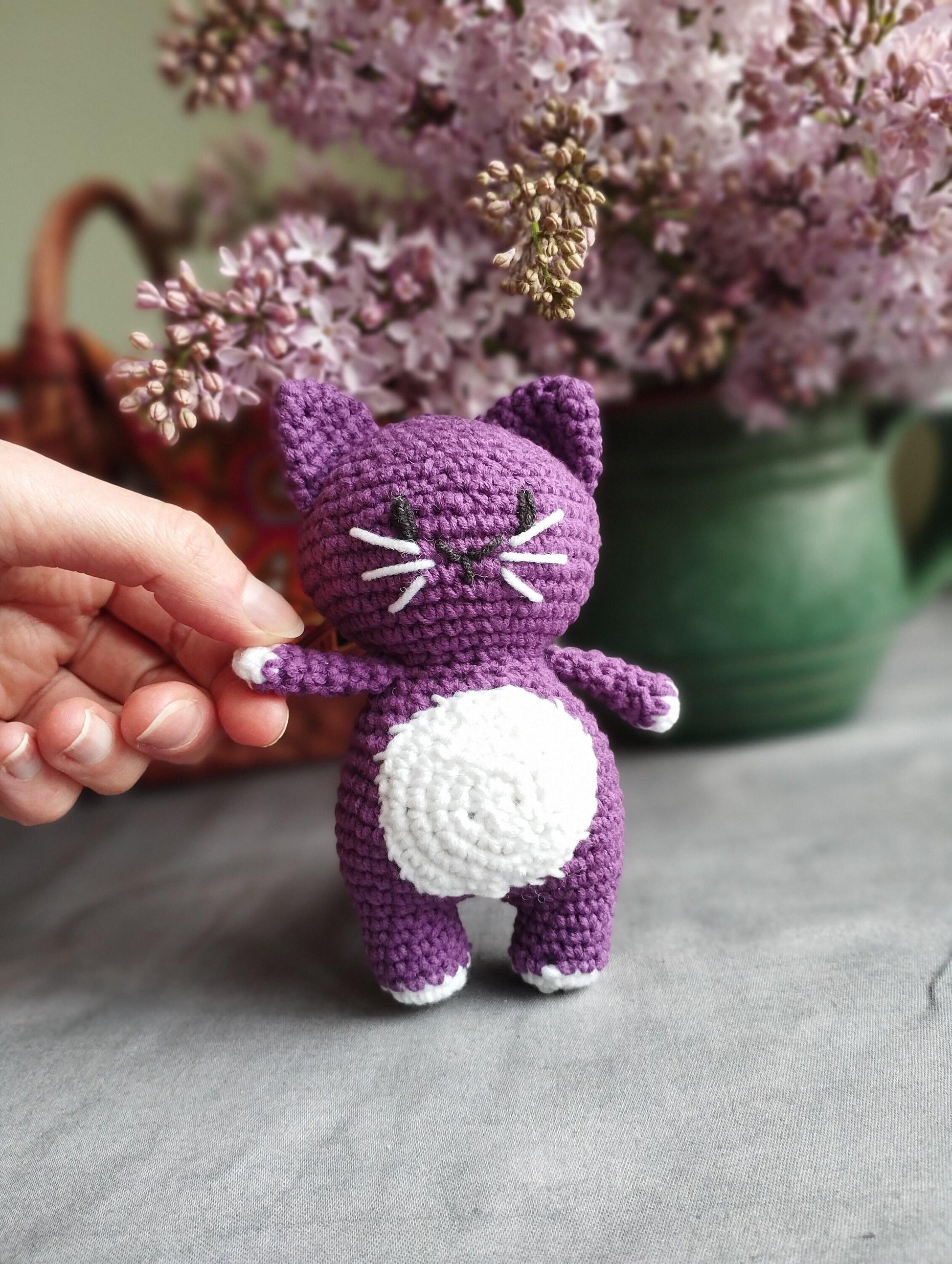 a person is holding a small crocheted cat