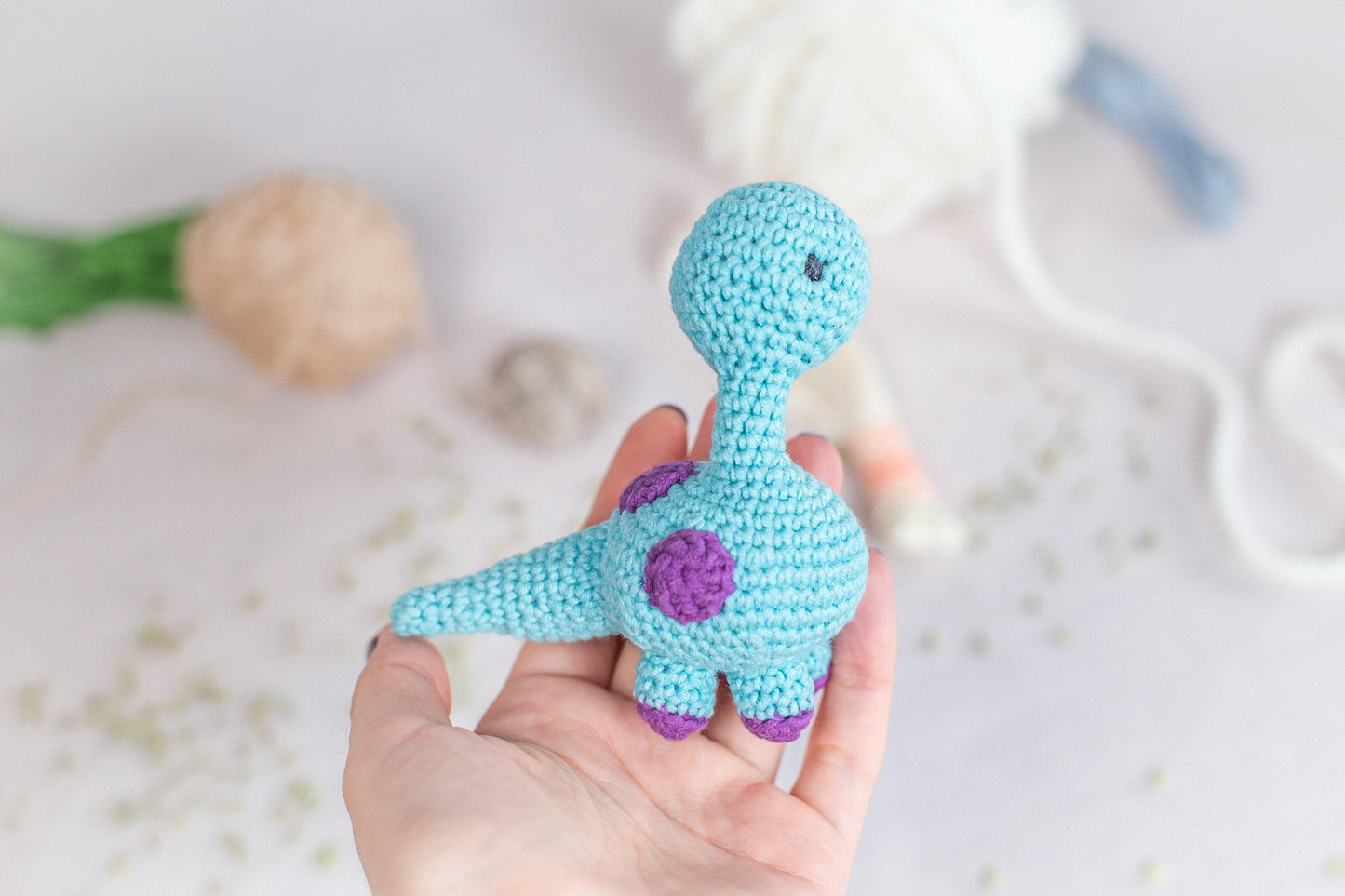 a hand holding a crocheted toy in front of a ball of yarn