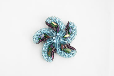 a blue flower brooch sitting on top of a white table
