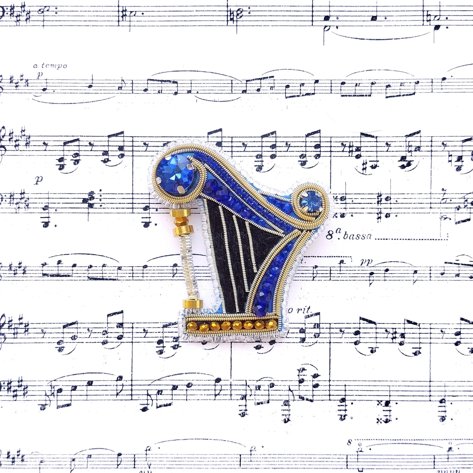 A blue and gold brooch with a black and white design is placed on top of sheet music.