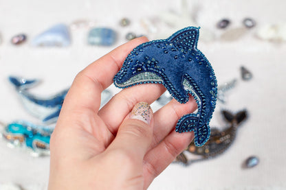 A hand holding a blue, beaded dolphin-shaped object against a background of various other beaded objects.