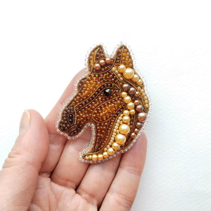 A hand holding a decorative piece of embroidered or beaded artwork depicting a horse's head.