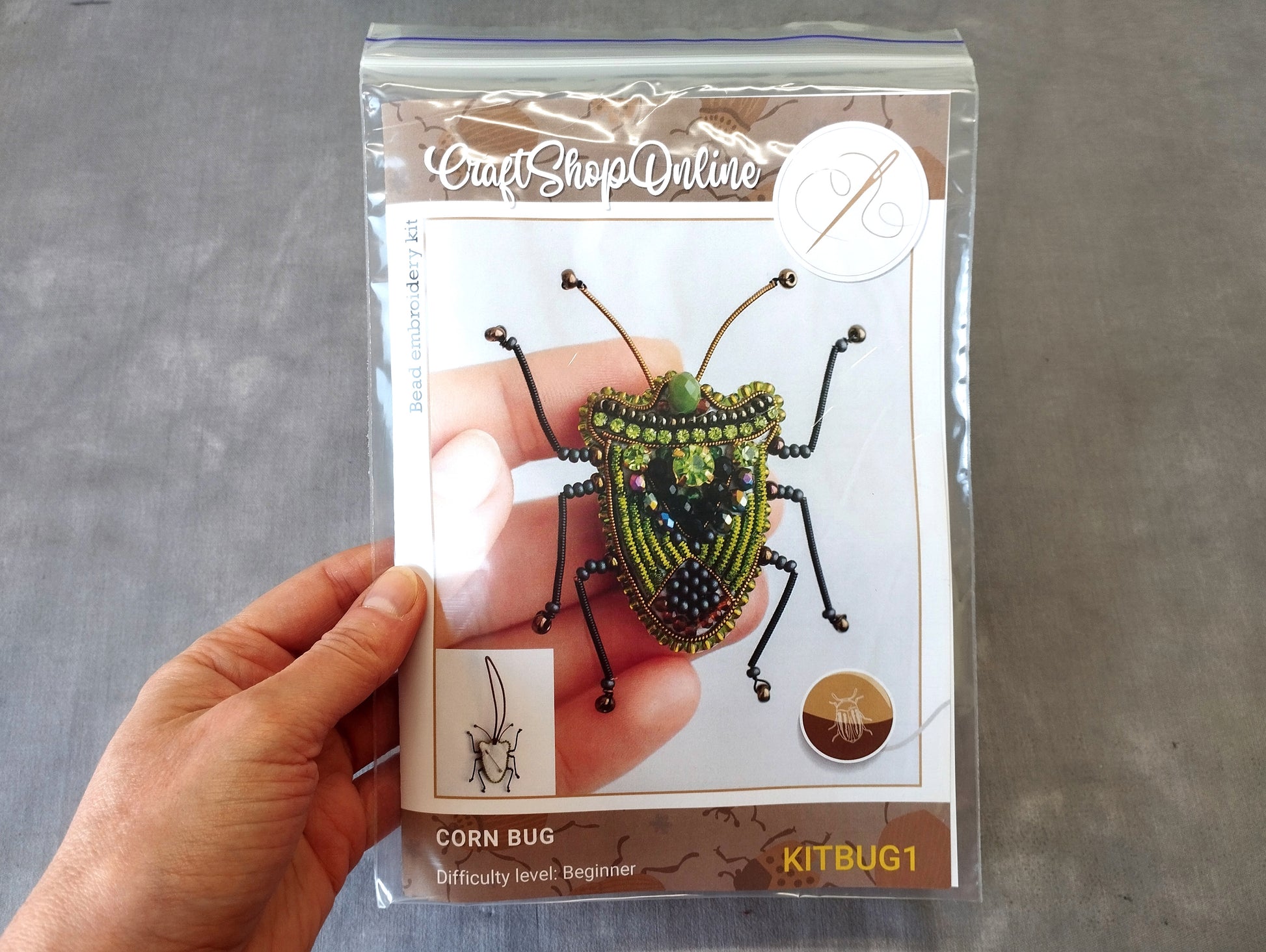 A hand holding a package containing a kit for creating a corn bug, with a detailed image of the kit and instructions for creating the insect.