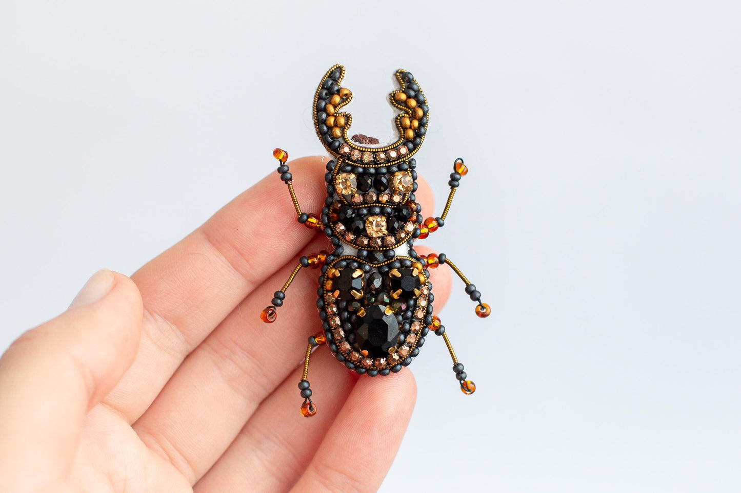 a hand holding a beaded bug on a white background